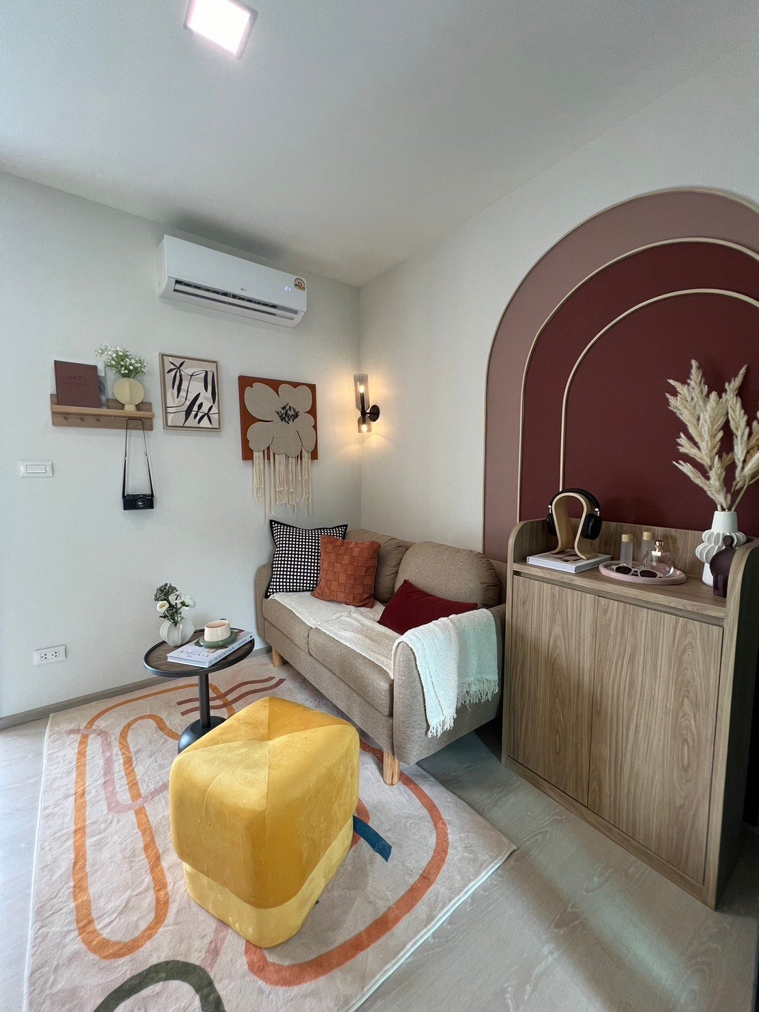 dcondo Calm: Living room with a beige sofa, colorful rug, and decorative wall arch feature.