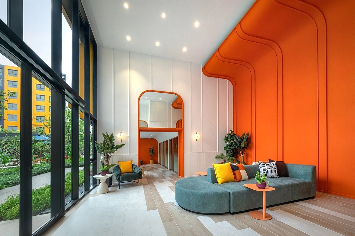 dcondo Shine Rangsit: Modern lounge at dcondo Shine Rangsit featuring a curved sofa and a striking orange accent wall.